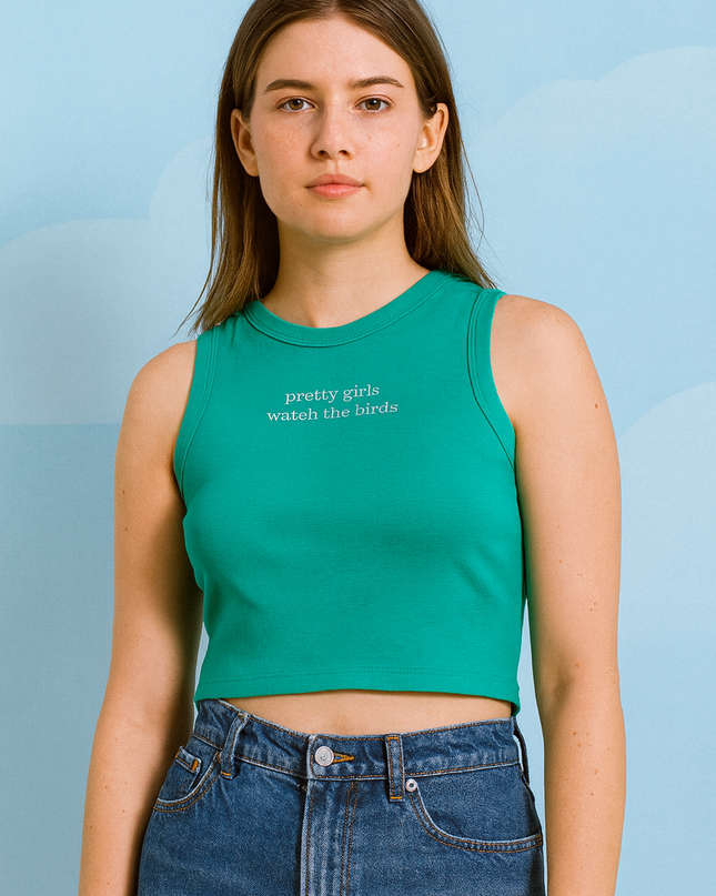 A young woman wearing a green crop top and blue jeans stands against a blue sky background.