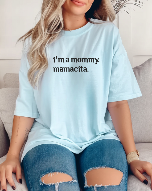 A woman wearing a light blue t-shirt with the text "I'm a mamma. mamatica." is sitting on a couch.