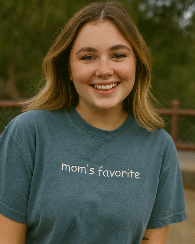 A smiling young woman wearing a blue t-shirt with the text "Mom's favorite" printed on it.
