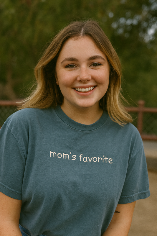 A smiling young woman wearing a blue t-shirt with the text "Mom's favorite" printed on it.