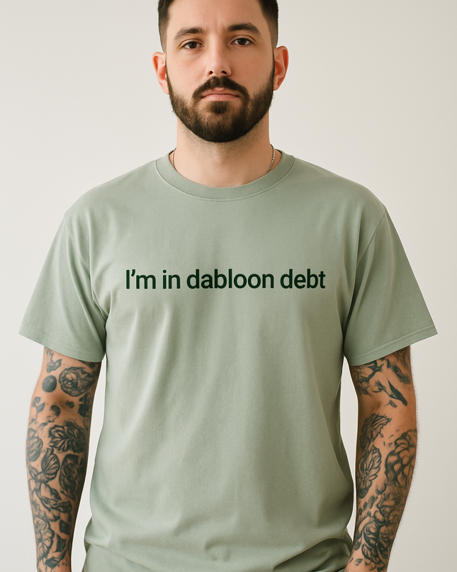 A man with a beard wearing a green t-shirt with the text "I'm in dabloon debt" printed on it.