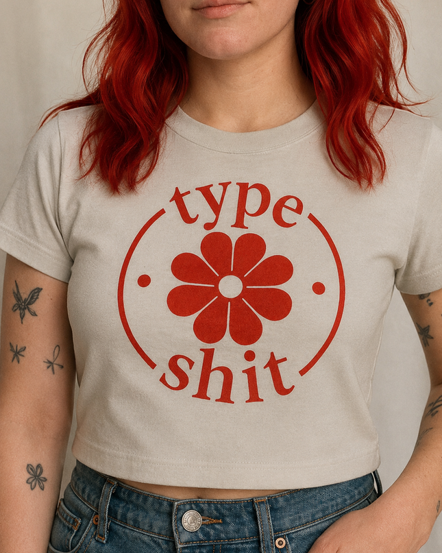 A woman with red hair wearing a white t-shirt with a red flower graphic and the text "type shit" printed on it.