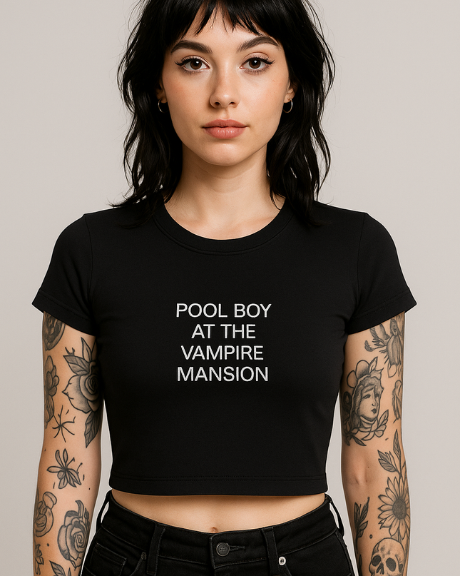 A young woman with dark hair and tattoos on her arms is wearing a black crop top with the text "POOL BOY AT THE VAMPIRE MASSION" printed on it.