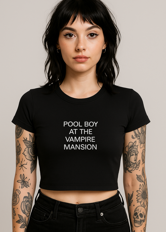 A young woman with dark hair and tattoos on her arms is wearing a black crop top with the text "POOL BOY AT THE VAMPIRE MASSION" printed on it.