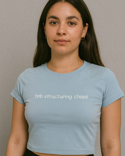 A young woman with long dark hair wearing a light blue crop top with the text "brb structuring chaos" printed on it.