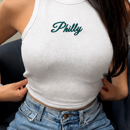 A woman wearing a white tank top with the word "Philly" printed on it, paired with blue jeans.