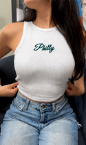 A woman wearing a white tank top with the word "Philly" printed on it, paired with blue jeans.