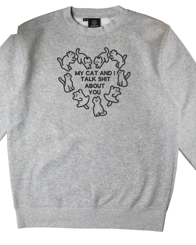 A gray sweatshirt with a black graphic design on the front. The design features a heart shape with the text "MY CAT AND I TALK SHIT ABOUT YOU" written inside it.