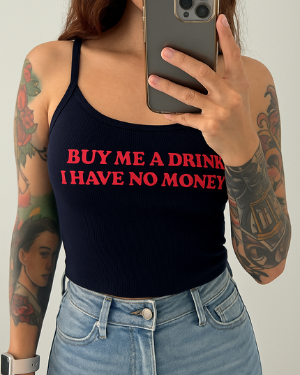 A person with tattoos on their arms is taking a selfie with a smartphone, wearing a black tank top with the text "BUY ME A DRINK I HAVE NO MONEY" printed on it.