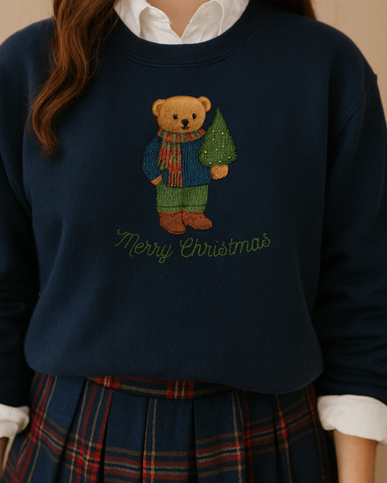 A woman wearing a navy blue sweater with a teddy bear embroidered on it, holding a Christmas tree, and a white collared shirt.