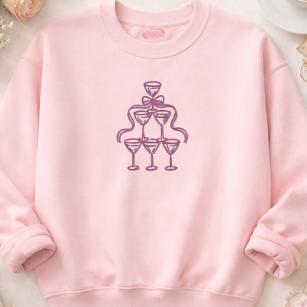 A pink sweatshirt with a graphic design of a stylized champagne glass and a ribbon on the front.