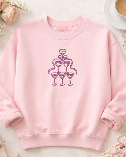 A pink sweatshirt with a graphic design of a stylized champagne glass and a ribbon on the front.
