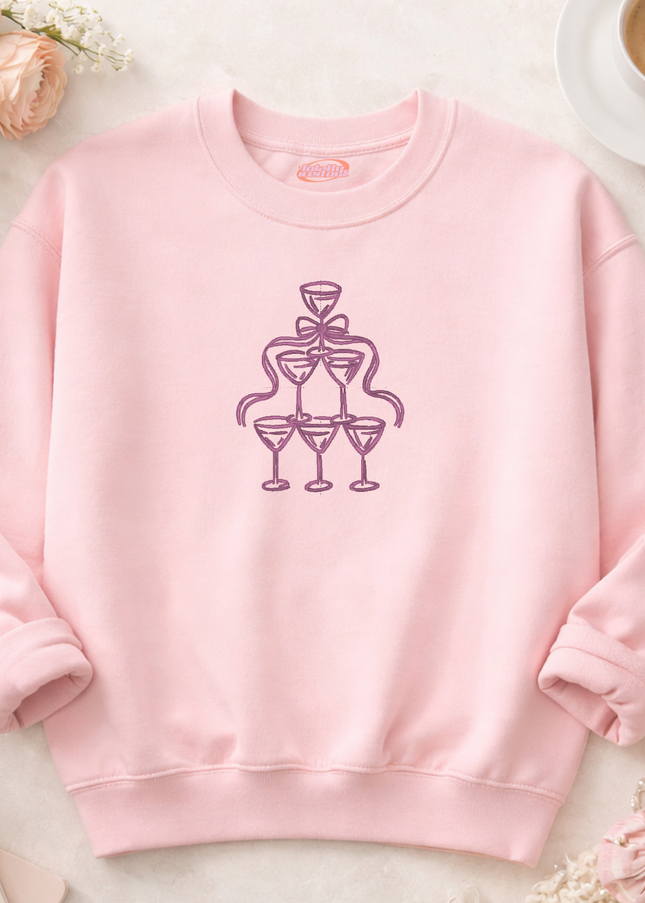 A pink sweatshirt with a graphic design of a stylized champagne glass and a ribbon on the front.