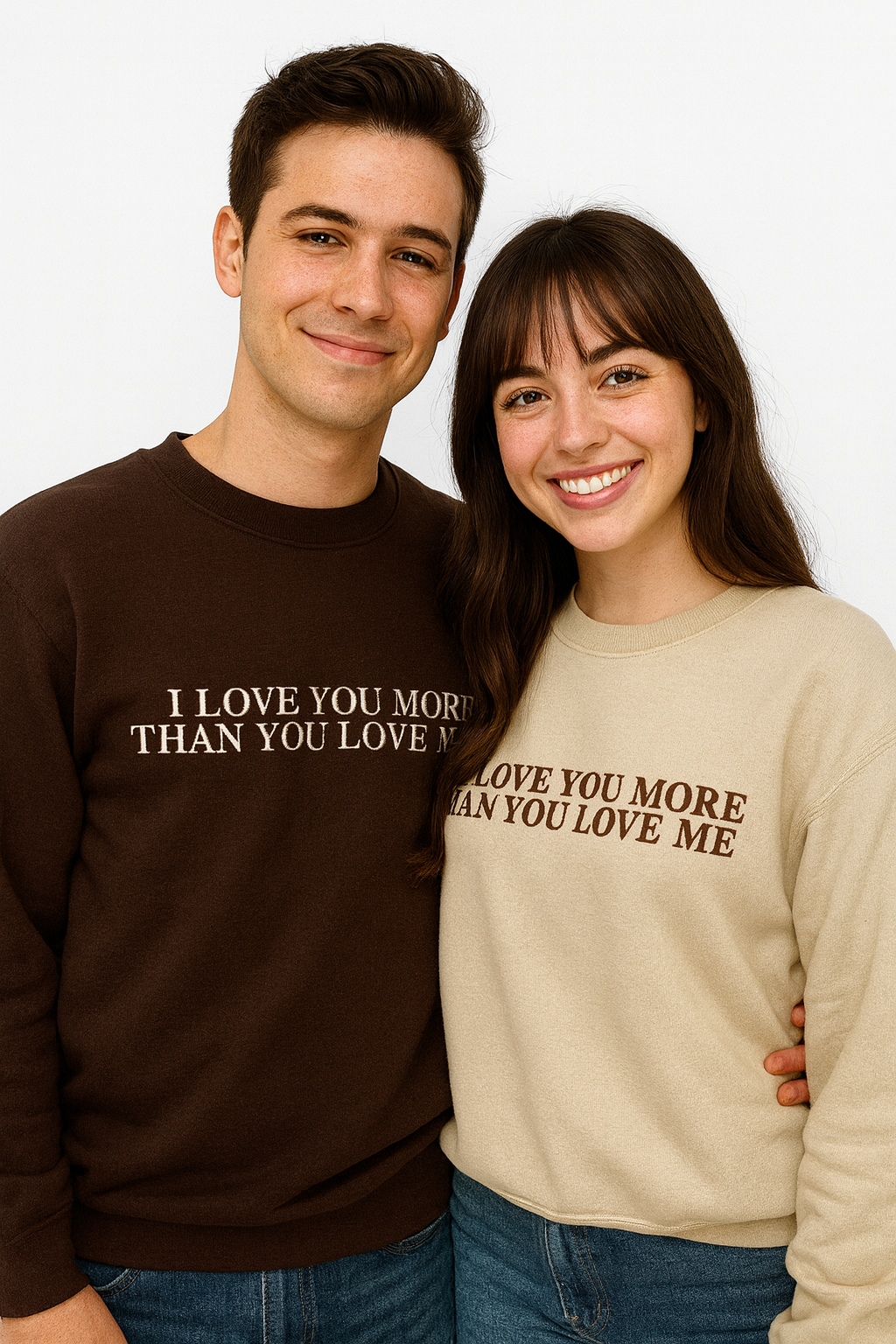 A man and a woman standing next to each other, both smiling and wearing matching sweaters with the text "I LOVE YOU MORE THAN YOU LOVE ME" printed on them.