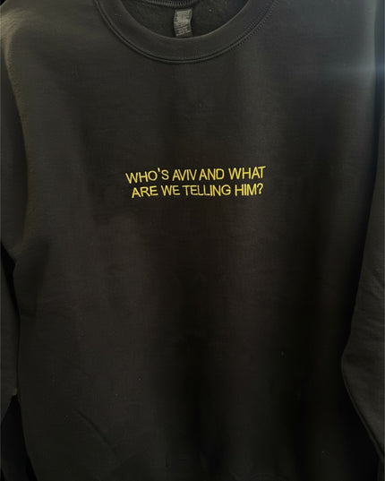 A black sweatshirt with the text "WHO'S AVIV AND WHAT ARE WE Telling HIM?" printed on it in yellow.
