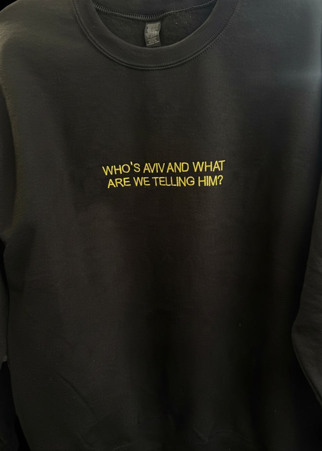 A black sweatshirt with the text "WHO'S AVIV AND WHAT ARE WE Telling HIM?" printed on it in yellow.