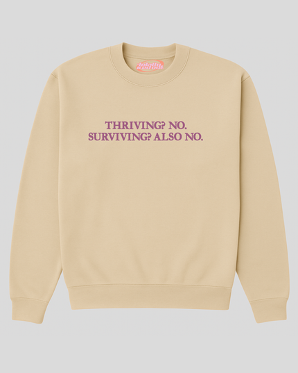 A beige sweatshirt with the text "THRIVING? NO SURVIVING? ALSO NO" printed on it in purple.