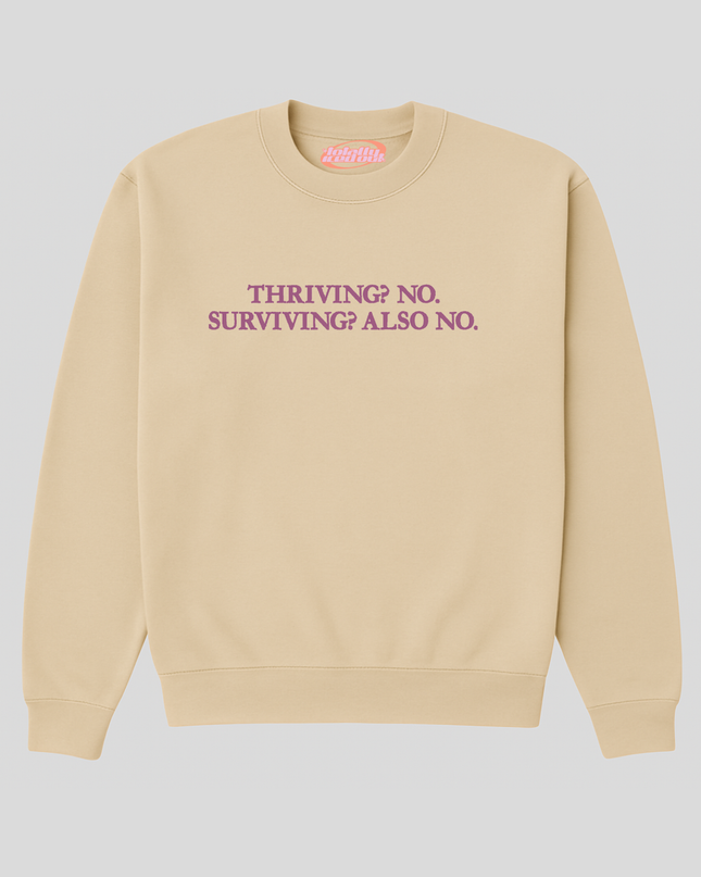 A beige sweatshirt with the text "THRIVING? NO SURVIVING? ALSO NO" printed on it in purple.