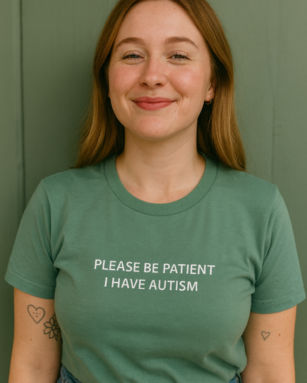 A woman wearing a green t-shirt with the text "PLEASE BE PATIENT I HAVE AUTISM" printed on it, smiling at the camera.