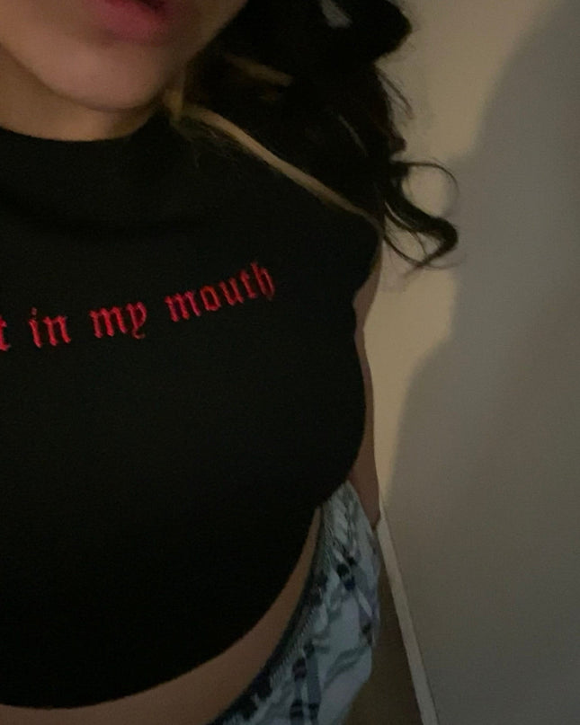 A person wearing a black top with the text "Spit in my mouth" printed on it.
