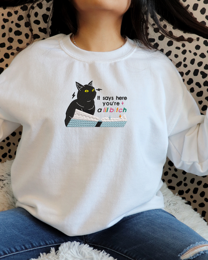 A person wearing a white sweatshirt with a graphic of a cat and text printed on it.