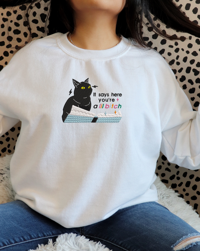 A person wearing a white sweatshirt with a graphic of a cat and text printed on it.