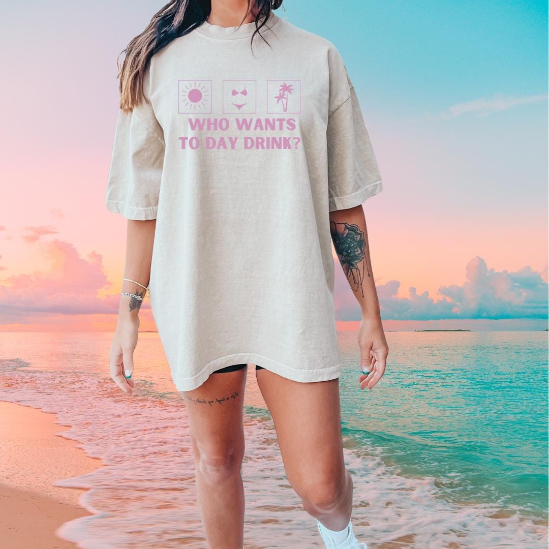 a woman standing on the beach wearing a shirt that says who wants to day drink