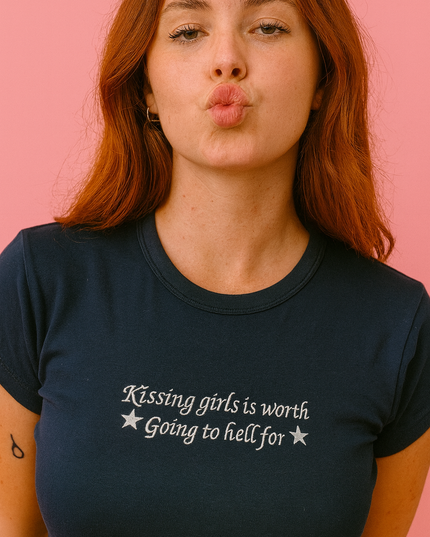 A woman with long red hair wearing a navy blue t-shirt with the text "Kissing girls is worth going to hell for" printed on it.