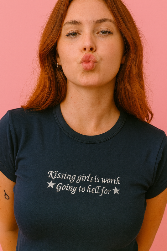 A woman with long red hair wearing a navy blue t-shirt with the text "Kissing girls is worth going to hell for" printed on it.