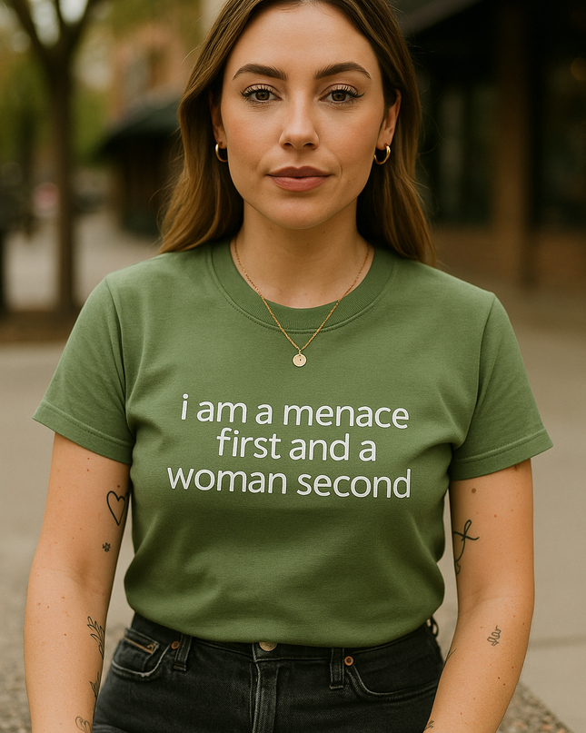 A woman wearing a green t-shirt with the text "I am a manace first and a woman second" stands in front of a building.