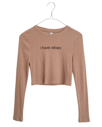 A beige long-sleeved shirt with the text "I have Rabies" printed on it, hanging on a metal hanger.