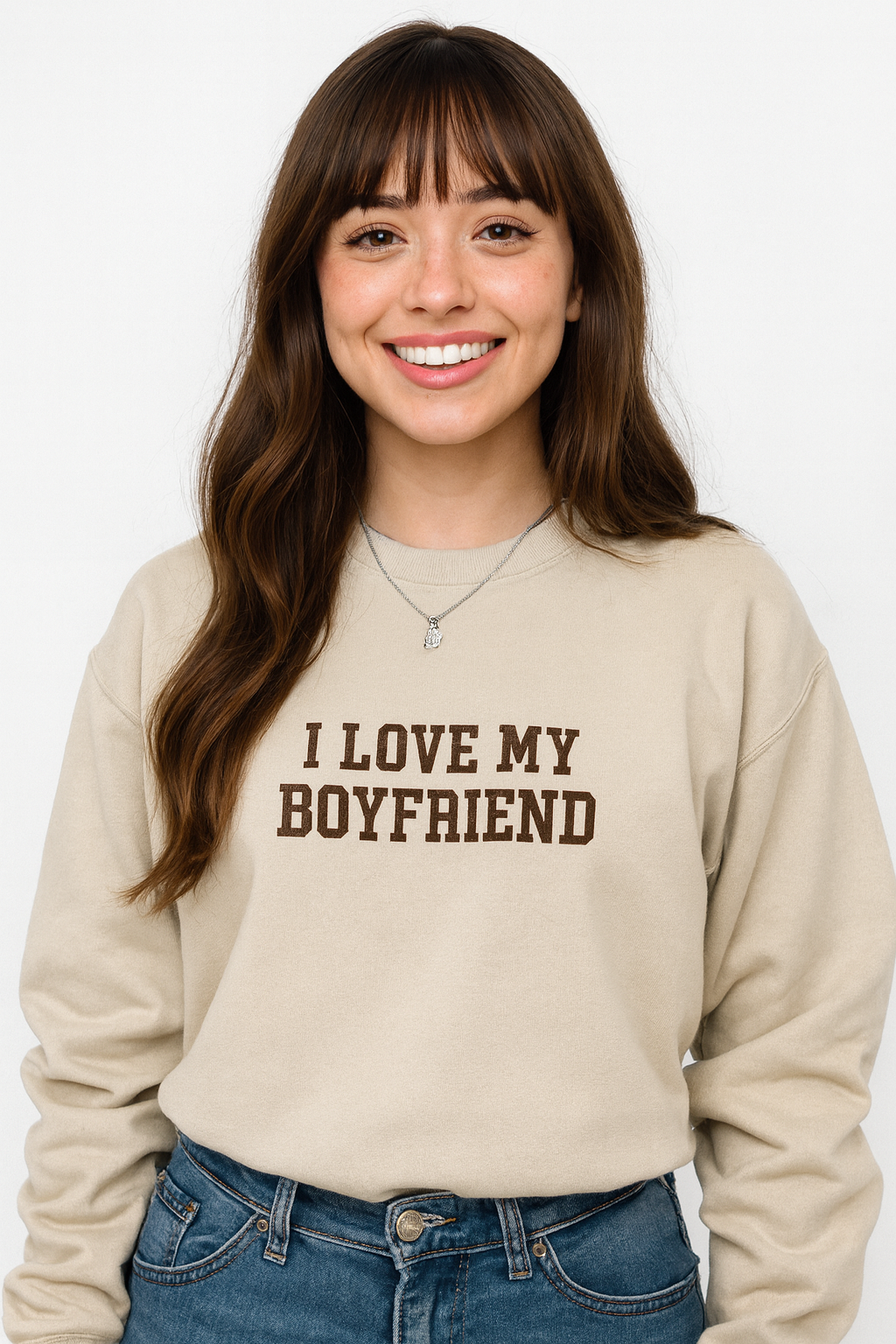 A smiling woman with long brown hair wearing a beige sweatshirt with the text "I LOVE MY BOYFRIEND" printed on it.