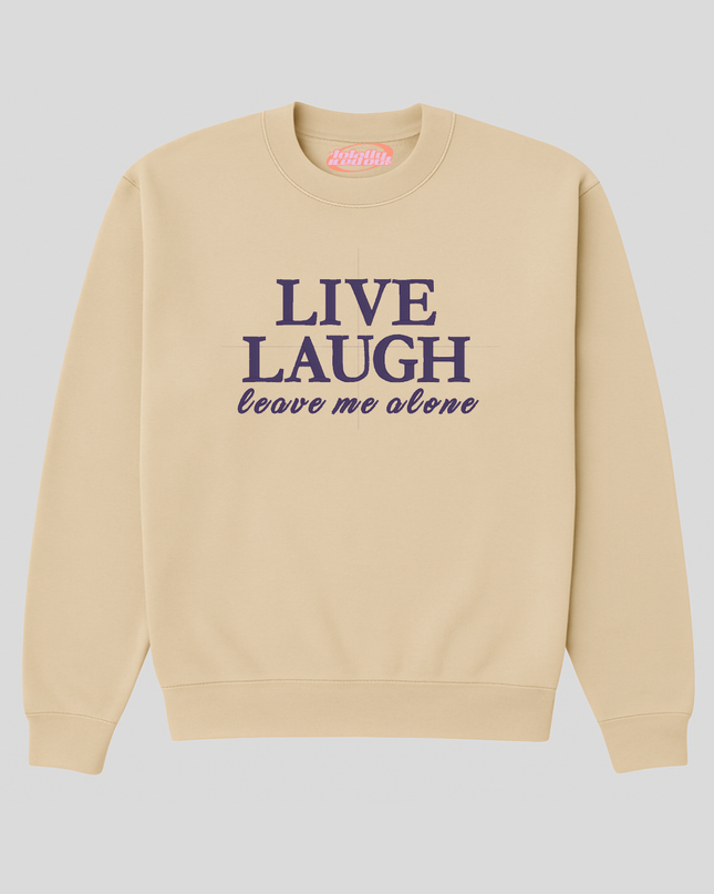 A beige sweatshirt with the text "LIVE LAUGH leave me alone" printed on it in purple.