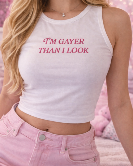A woman wearing a white crop top with the text "I'm gay than I look" printed on it, paired with pink jeans.