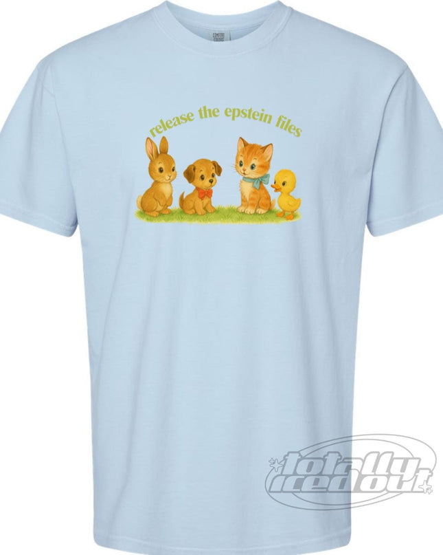 A light blue t-shirt with a graphic design featuring a rabbit, a dog, a cat, and a bird on a grassy field. The text above the image says "release the Epstein files".