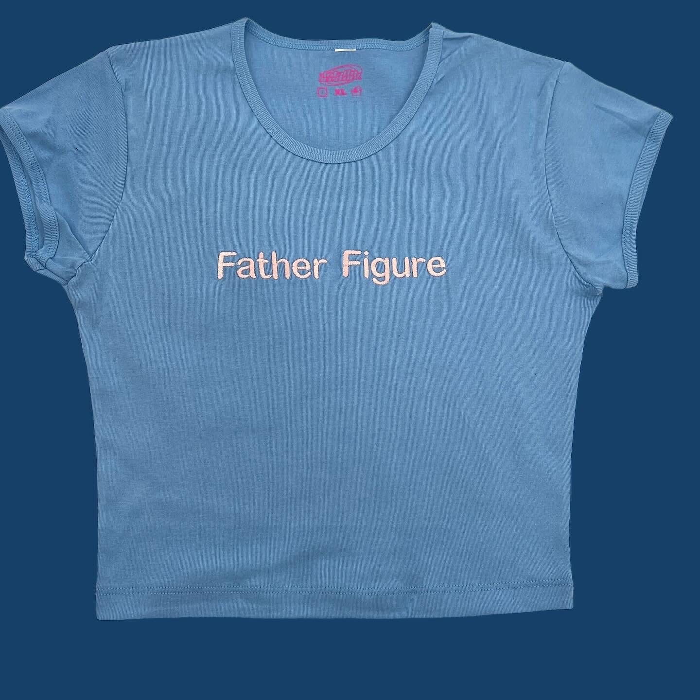A light blue t-shirt with the text "Father Figure" printed on it.