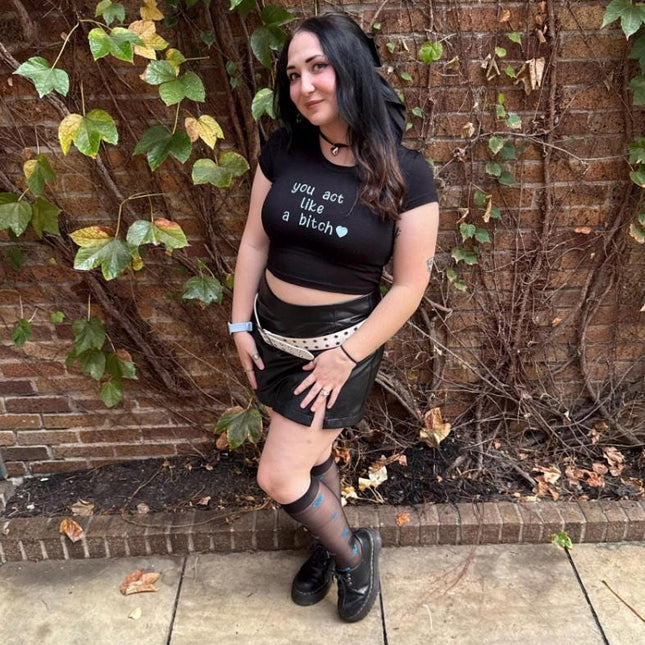 a woman in a black shirt and skirt posing in front of a brick wall