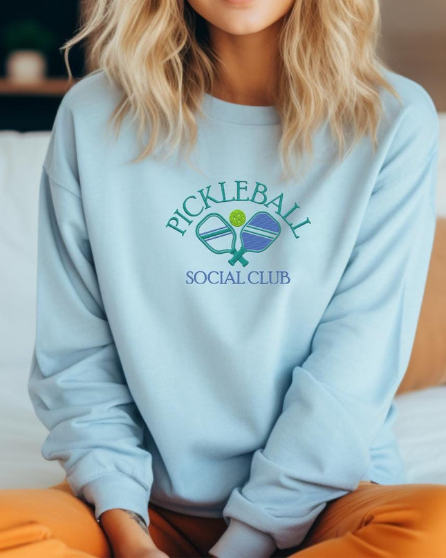 a woman sitting on a bed wearing a blue sweatshirt