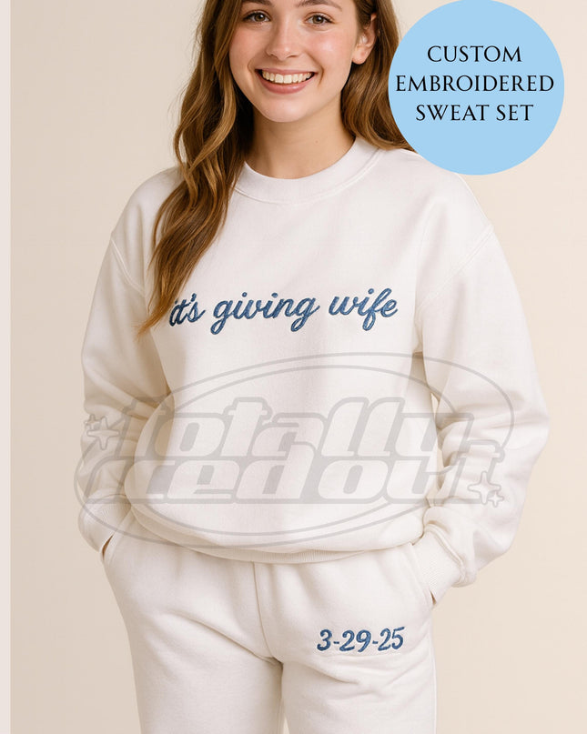 A smiling woman wearing a white sweatshirt with the text "It's giving wife" embroidered on it.