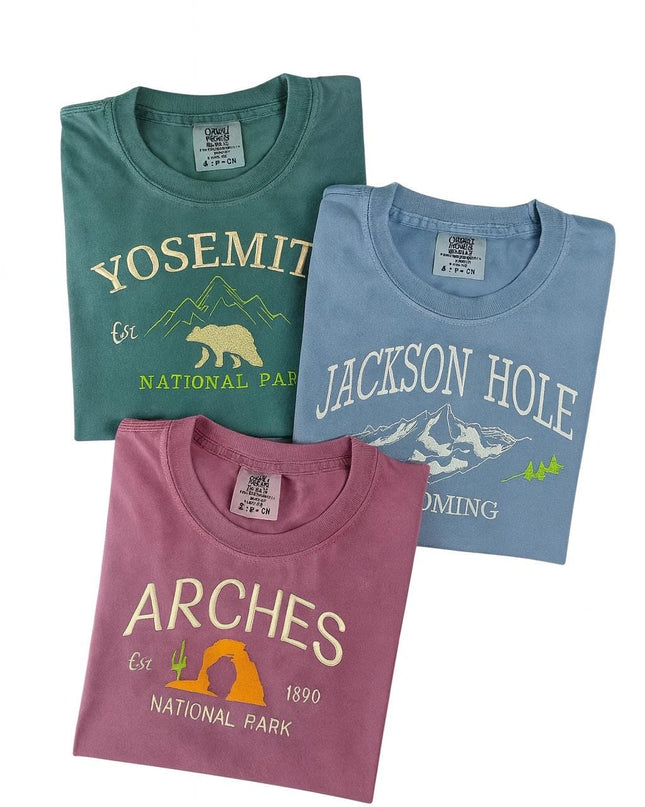 Three t-shirts with different mountain landscapes printed on them, including Yosemite, Jackson Hole, and Arches National Park.