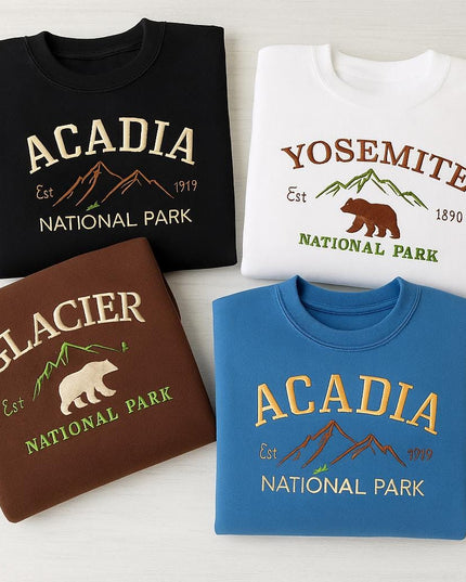 four different sweatshirts or t-shirts, each with a unique design and color, representing different national parks in the United States.