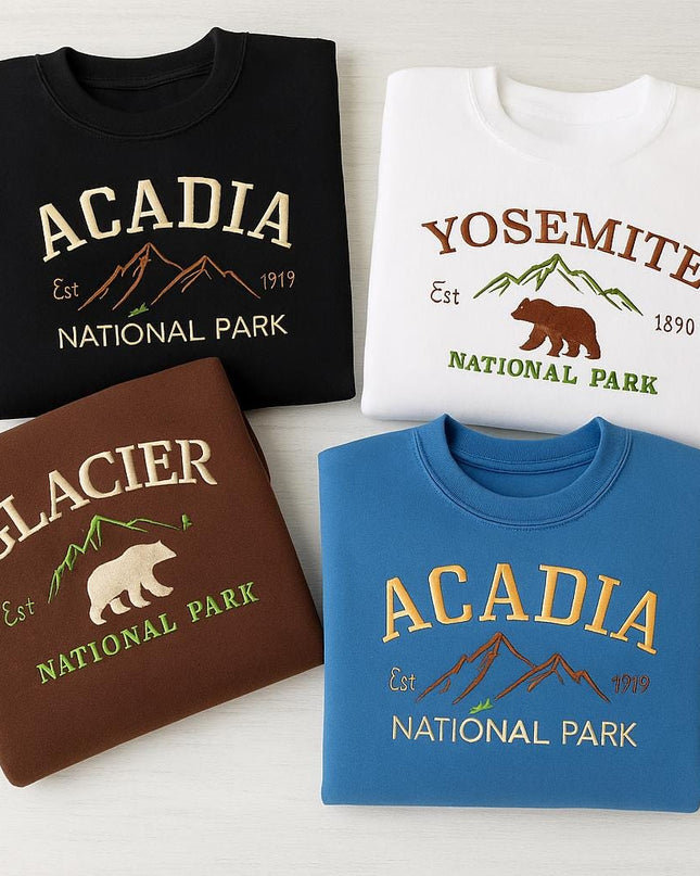 four different sweatshirts or t-shirts, each with a unique design and color, representing different national parks in the United States.